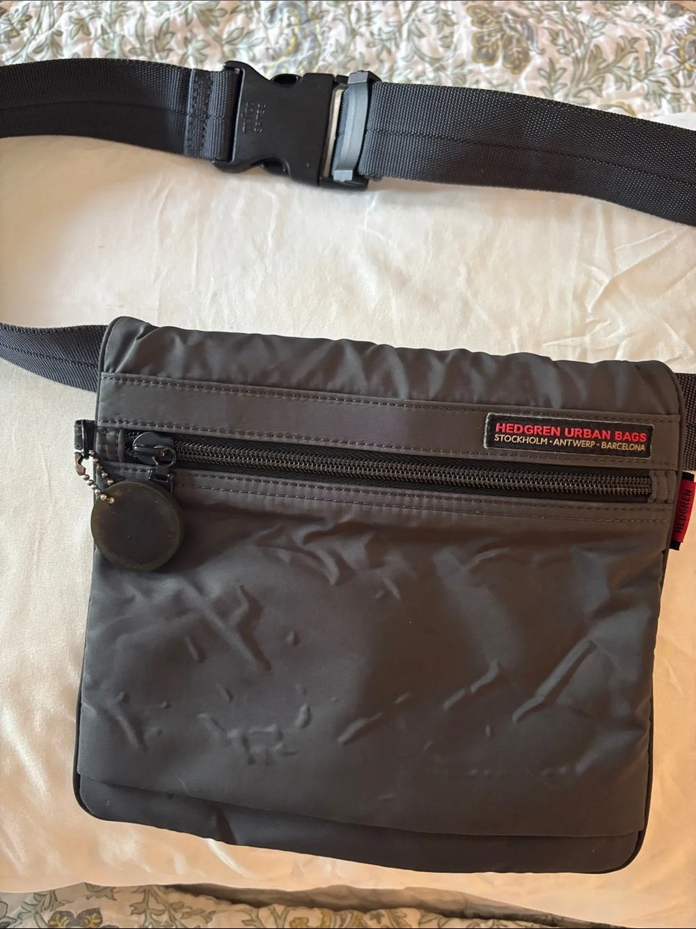 This grey Hedgren crossbody bag features a distinctive red label showcasing the